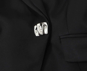 Detail shot of a black cropped blazer featuring a textured silver irregular metal button