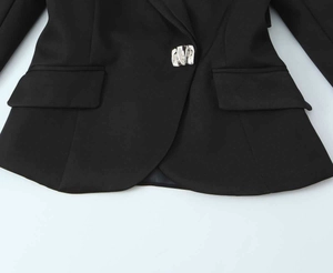 Detail of black short blazer featuring a textured irregular silver metal button closure