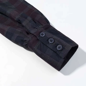 Detalle del puño de camisa a cuadros con tres botones oscuros y pliegues en tela gris oscura