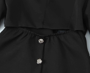 Detail of black cropped blazer featuring cutout design and silver textured metal buttons