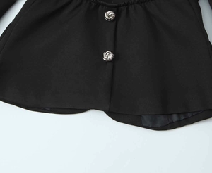 Detail of black cropped blazer hem featuring two silver spiral decorative buttons
