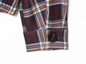 Détail du poignet d'une veste à carreaux rouge et bleu avec bouton noir poli et couture fine