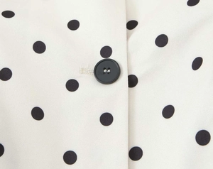 Detailed close-up of a black button and polka dot pattern on an off-white blazer