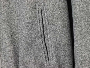 Close-up of a grey wool blend jacket detail showing a vertical welt pocket and fine stitching