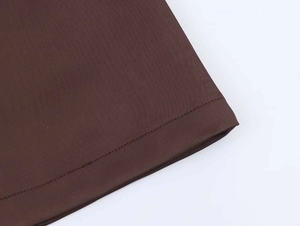 Macro detail of brown dress hem showing high-quality woven fabric and neat topstitching