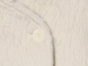 Macro shot of fluffy cream faux fur texture and a matching four-hole button on the jacket