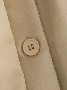Macro shot of beige gathered jacket with matching four-hole button and fine twill texture