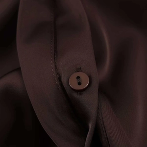 Detail of a dark chocolate satin shirt showing polished buttons and fine twill texture