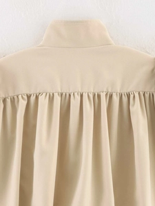 Detail view of beige ruched jacket featuring elegant back pleats and stand collar design