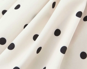 Close-up of ivory white fabric with black polka dots showing smooth texture and drape