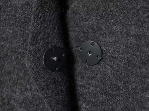 Close-up of black metal snap button on dark grey wool blend knit fabric texture