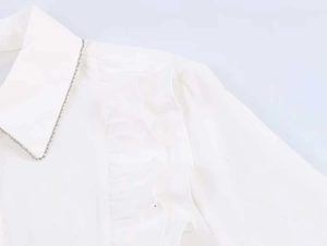 Detail showing white poplin shirt with vertical ruffles and elegant lapel collar