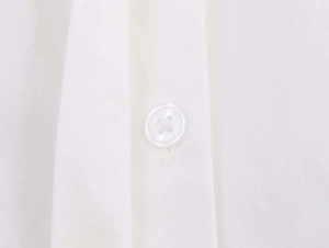 Close-up of white poplin shirt detailing a classic four-hole button on plain fabric