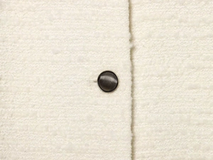 Détail du tissu en tweed ivoire et bouton métallique rayé sur la veste à manches longues