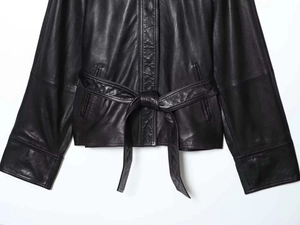 Detailed close-up of a black faux leather jacket featuring a waist belt and side pockets