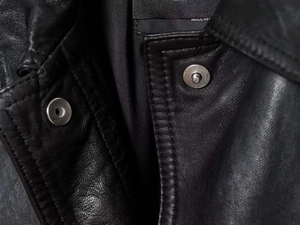 Macro shot of black leather jacket neckline with metallic snap buttons and fine texture