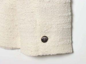 Gros plan d'un bouton noir et doré sur la texture d'une veste en tweed blanc cassé