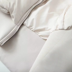 Detail of metal zipper closure and ribbed hem on a cream padded jacket with silky lining