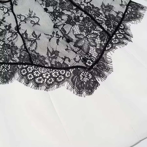 Close-up of black floral lace with eyelash trim stitched on white fabric dress