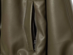 Dettaglio della tasca verticale con zip in metallo argento su giacca in finta pelle oliva