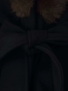 Detail of a black winter wool coat featuring a brown faux fur collar and bow belt