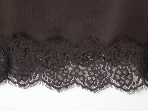 Detailed view of black eyelash lace trim stitched to smooth dark satin fabric