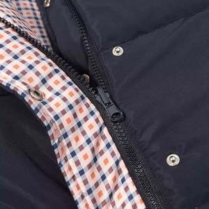 Detail of winter reversible jacket featuring blue nylon shell and plaid lining with metal buttons