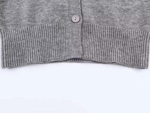 Detail of grey knitted cardigan featuring ribbed hem and matching round button closure