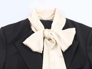Detail of a black blazer featuring a large cream satin bow with smooth silky texture