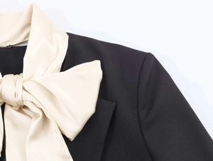 Detailed close-up of a black blazer with a large cream satin bow on the lapel