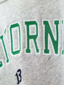 Detailed close-up of green letter embroidery and navy number on grey knitted sweatshirt