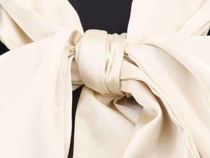 Macro view of cream satin bow detail with smooth silk texture on fashion blazer