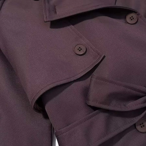 Gros plan d'un trench-coat bordeaux avec boutons classiques et coutures de précision