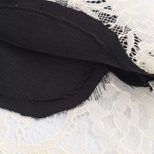Detailed view of black woven fabric stitched with delicate white floral lace trim