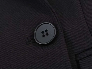 Detailed view of a matte black round button on a black twill fabric suit jacket