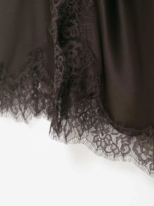 Detailed macro view of delicate eyelash lace trim on a dark brown silk satin dress hem