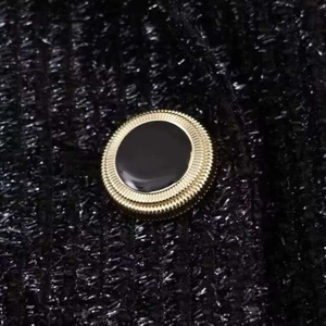 Dettaglio dei bottoni metallici dorati su blazer in tweed nero con trame strutturate