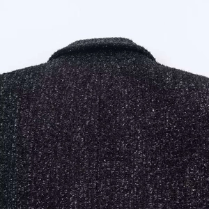 Dettaglio ravvicinato del retro del colletto di un blazer in tweed nero con trama tessuta