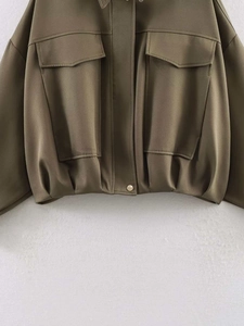 Close-up of military green bomber jacket with large flap pockets and pleated hem detail