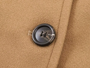 Macro detail of camel wool coat fabric featuring a dark tortoise shell resin button