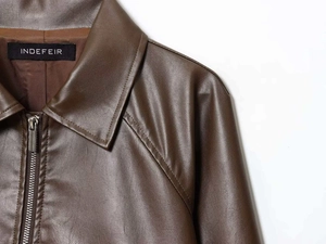 Detail of the brown leather jacket featuring the collar, zipper, and INDEFEIR brand label