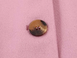Close-up of pink wool coat fabric with a dark brown tortoiseshell button and fine stitching