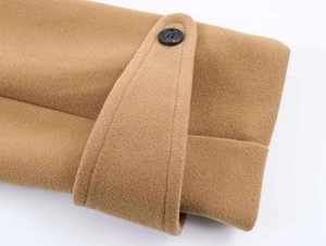 Close-up of camel wool coat sleeve featuring decorative strap and black button detail