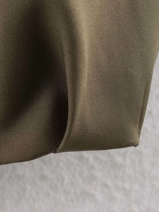 Close-up detail of dark olive bomber jacket fabric showing twill texture and hem stitching