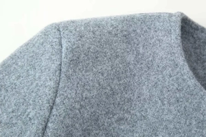 Detailed macro view of the grey wool blend fabric texture on the coat shoulder and collar