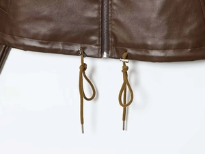 Detail view of brown faux leather jacket hem with silver zipper and drawstring tips