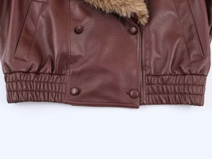 Detail of a brown leather jacket featuring a plush faux fur collar and textured finish