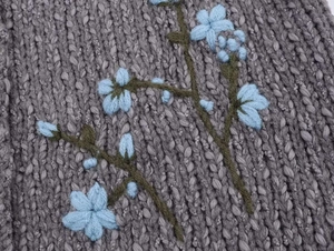 Close-up of delicate blue flower embroidery on grey knitted sweater fabric texture