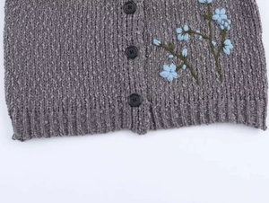 Detail of grey knit cardigan showing matte black buttons and blue floral embroidery