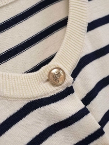 Detail of cream knit cardigan with navy stripes and a gold crest embossed button
